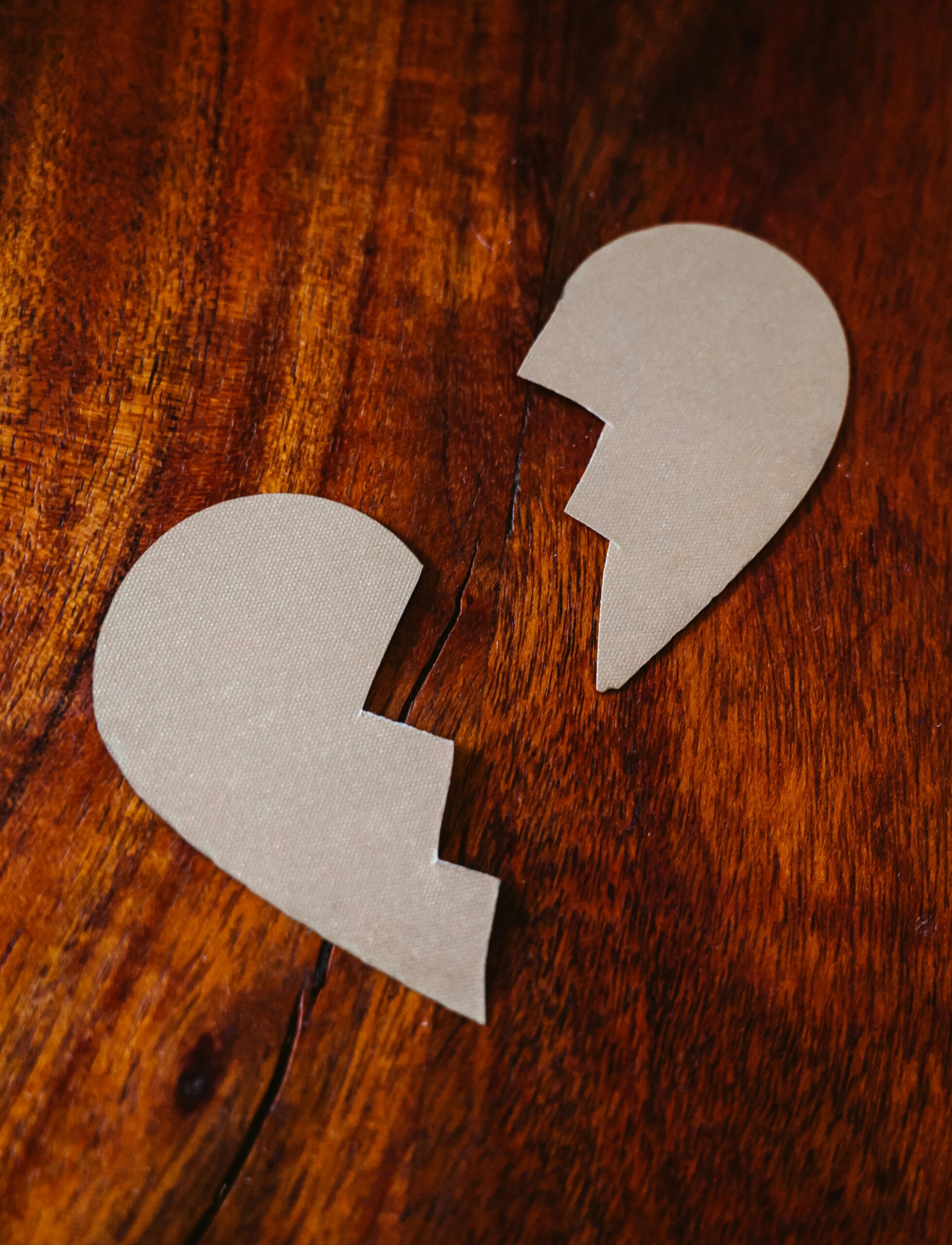 Cardboard broken heart symbol on wooden table, representing love and separation.